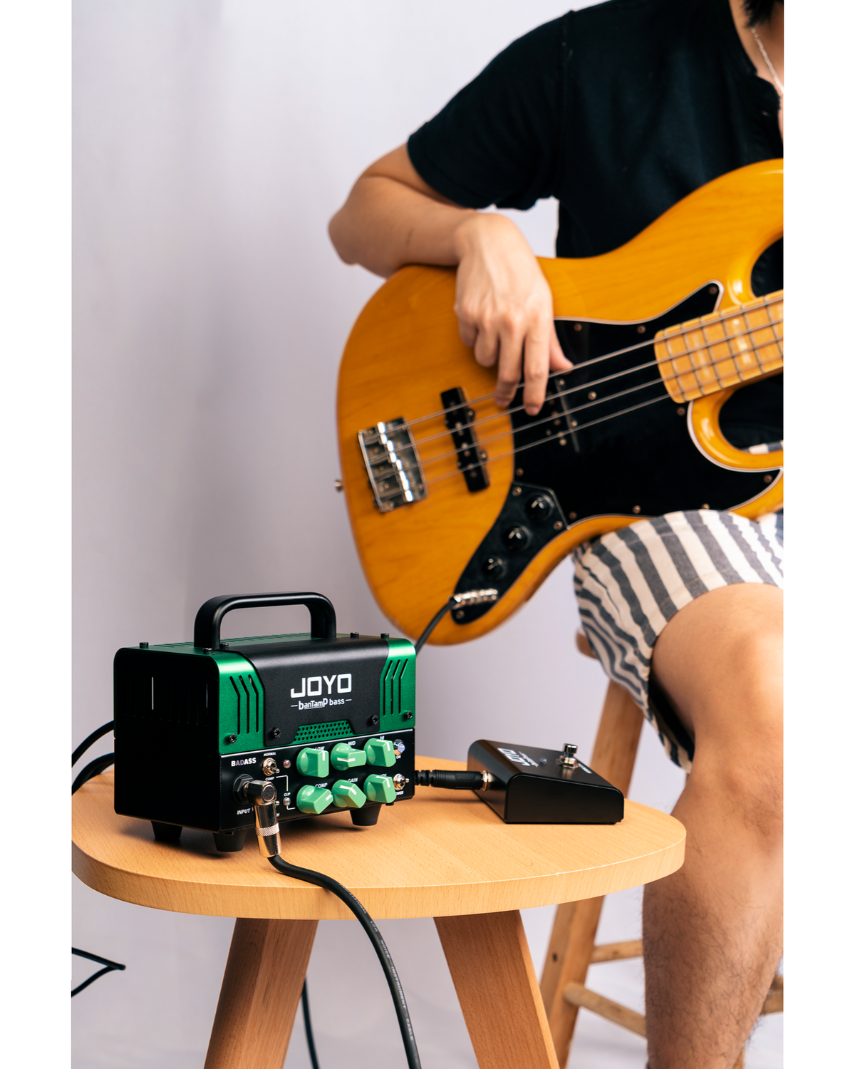 Haze Guitar Australia Joyo BADASS hybrid bass amp head with green controls and footswitch, played with a bass guitar.